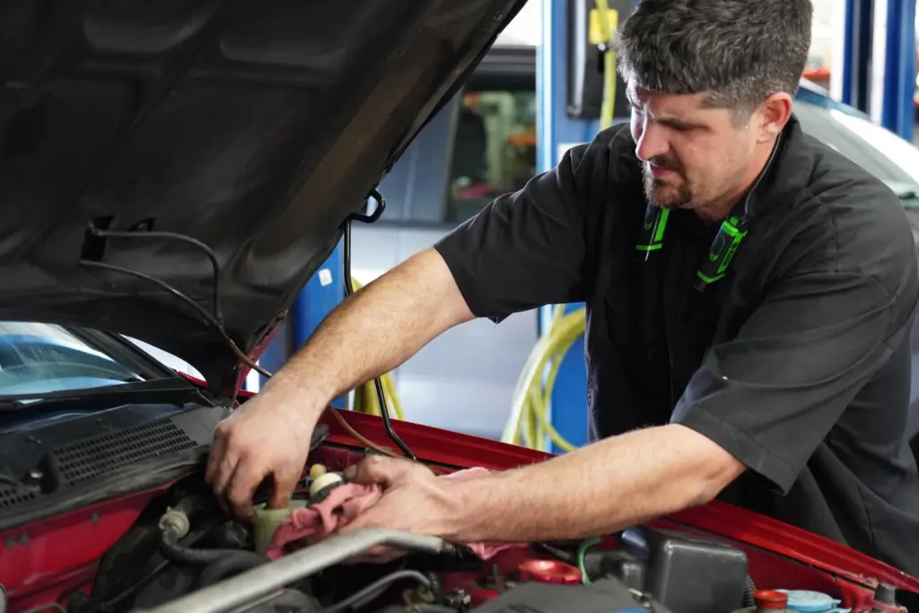 A mechanic works under the hood of a car in an auto repair shop in Panama City Beach, using a rag while inspecting the engine components.