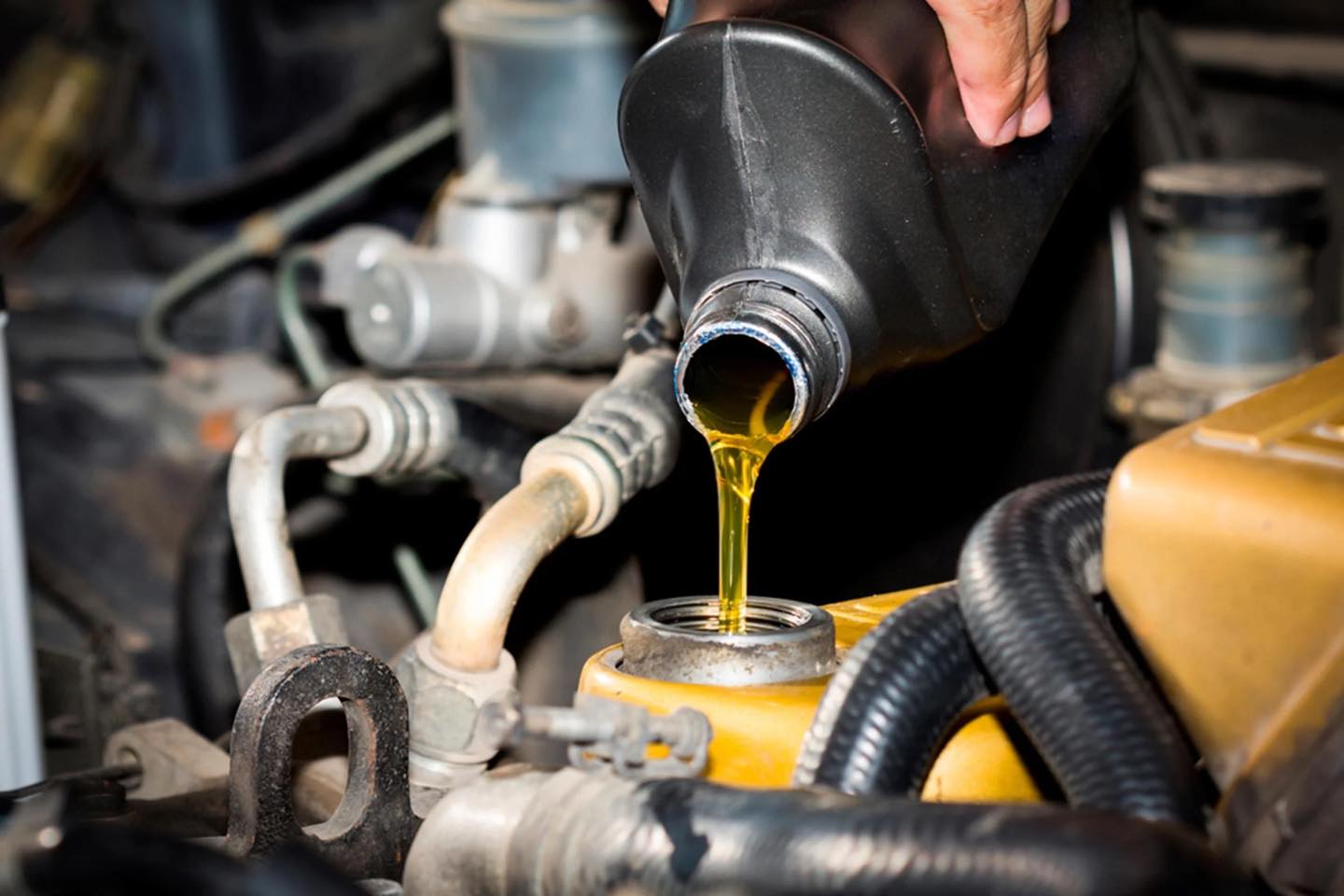 A mechanic pours engine oil from a black container into a car's engine oil filler port under the hood, showcasing expert auto repair in Panama City Beach.
