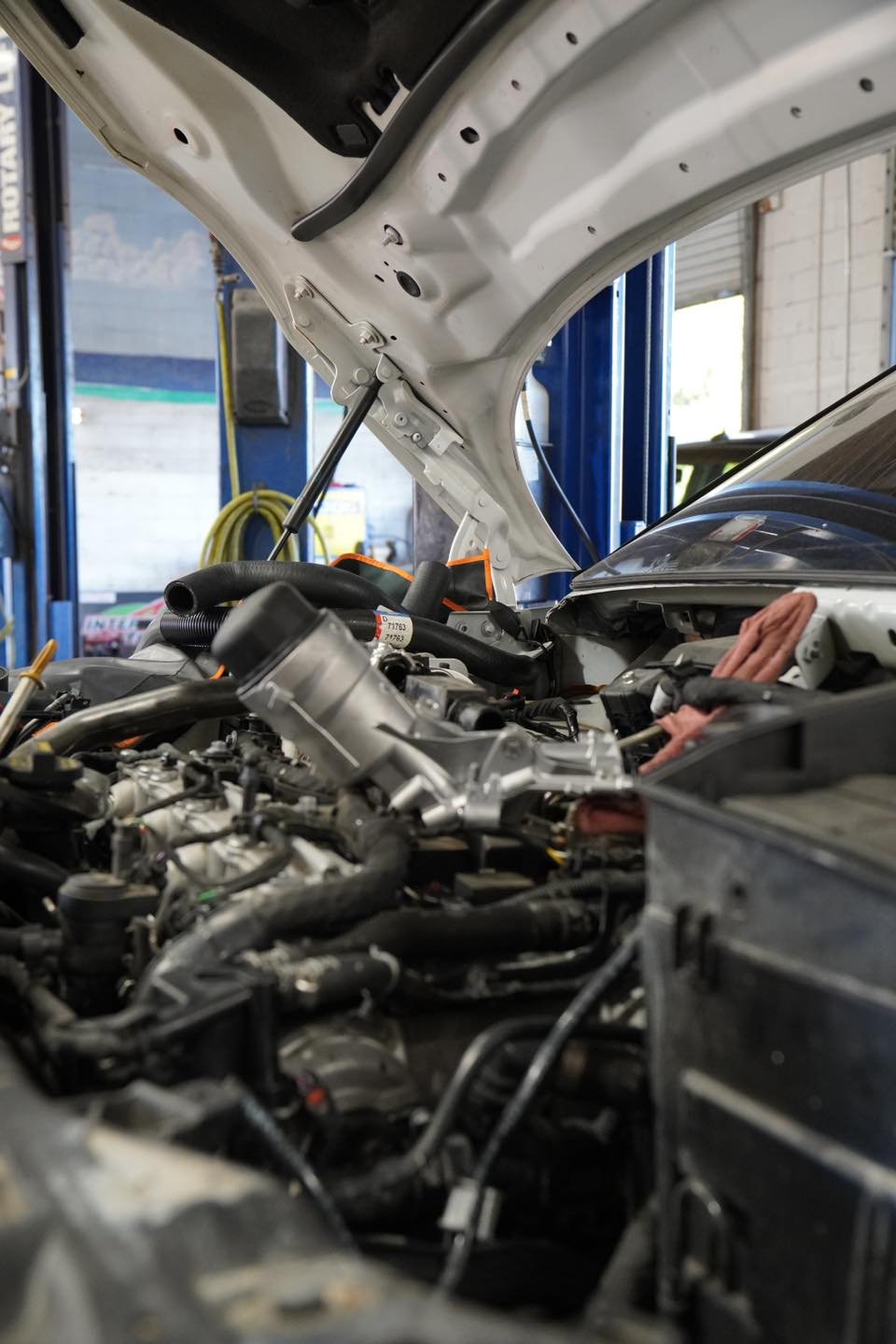 A close-up view of a car engine with the hood open inside a Panama City Beach car repair shop. Tools and hoses are visible around the engine bay.