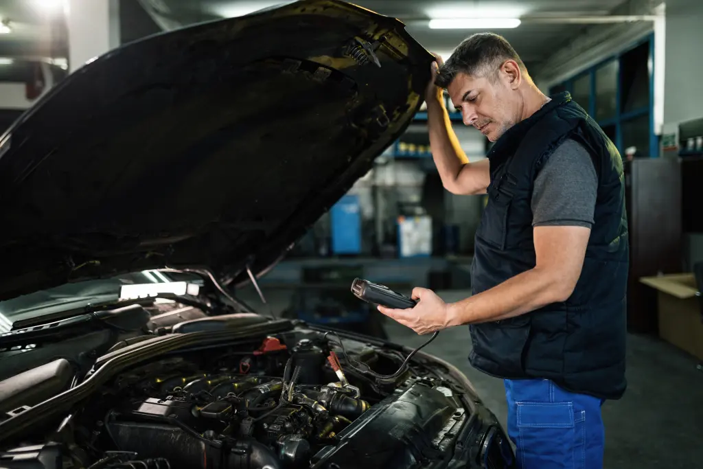 A mechanic in Panama City Beach stands next to an open car hood, holding a diagnostic tool and carefully inspecting the engine in a garage.