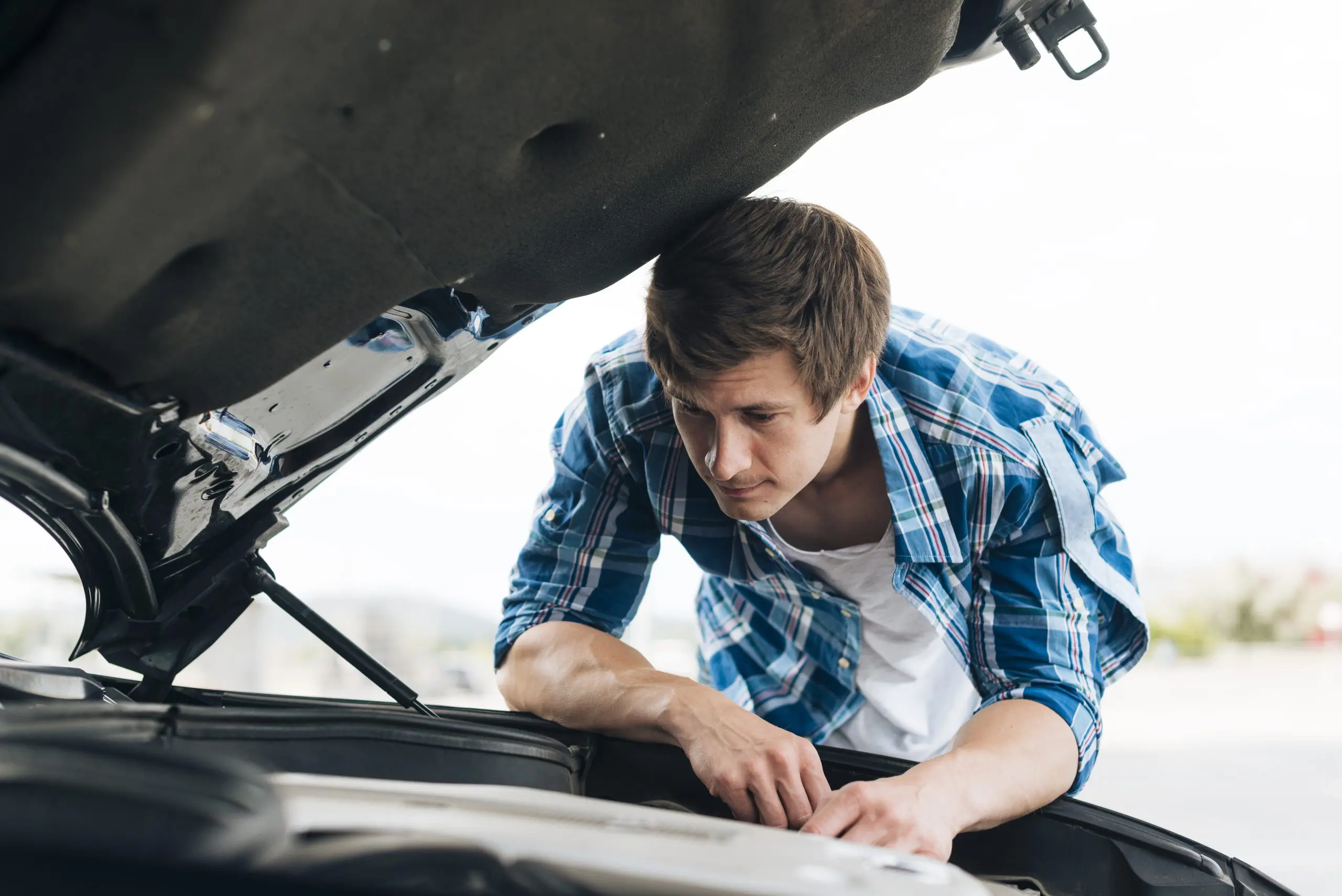 A man in a plaid shirt looks under the hood of a car at a Panama City Beach auto repair shop, inspecting the engine.