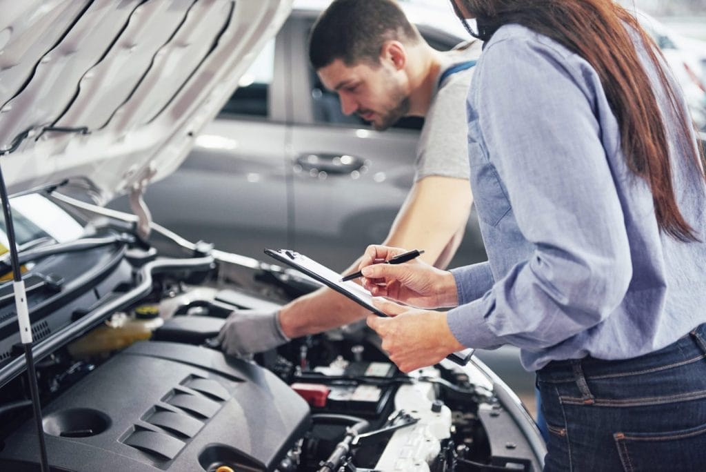 Mechanic and customer inspecting car engine.