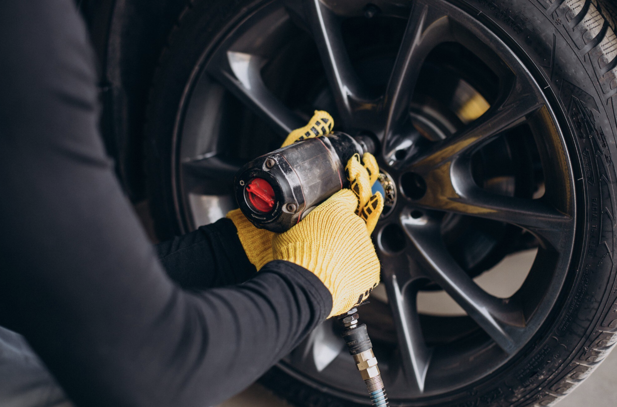 Person wearing yellow gloves uses a power tool to tighten or loosen lug nuts on a car wheel, an important step in tire rotation for better tire performance and longer tire life.