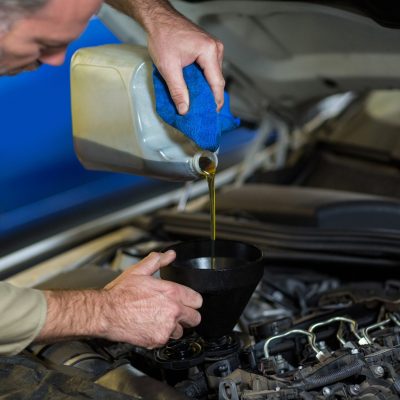 Mechanic pouring oil into car engine in repair garage