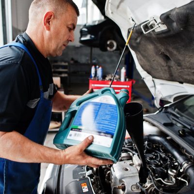 A mechanic pours engine oil into a car’s engine through a funnel under the open hood in an auto repair shop in Panama City Beach.